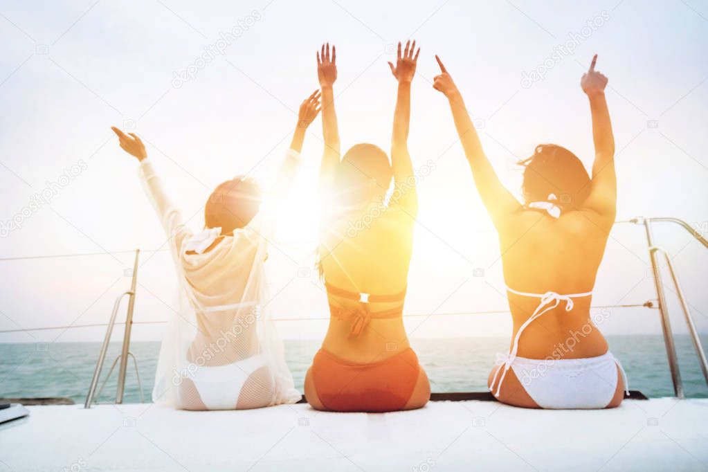 Three cheerful young women in bikini sitting on boat and admiring sea view