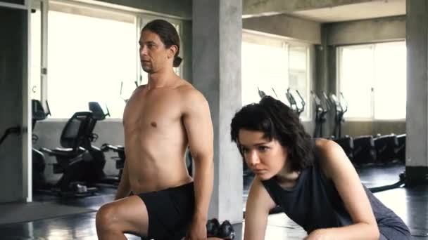 Młoda kobieta i mężczyzna rozprostowują nogi na podłodze sali gimnastycznej. Dwoje ludzi ćwiczy w domu. — Wideo stockowe