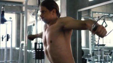 Gömleksiz kaslı adam spor salonunda göğüs egzersiz üzerinde kablo çapraz yapıyor.