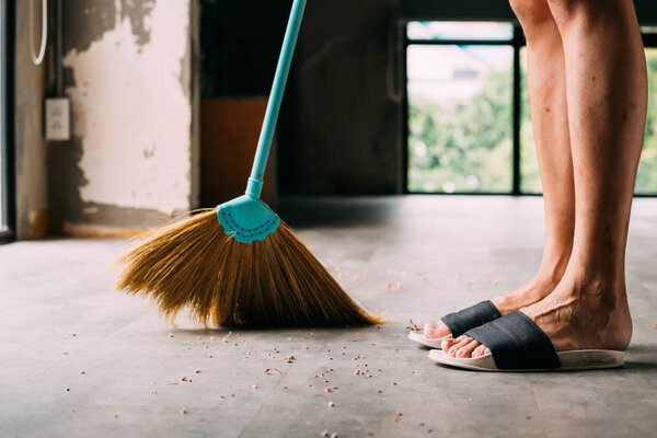 Human legs wearing slippers using sweeping broom inside the house