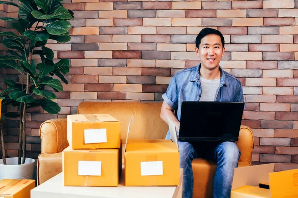 Asiatiska manliga företag entreprenör med hjälp av laptop med förpackningar med lådor hemma — Stockfoto