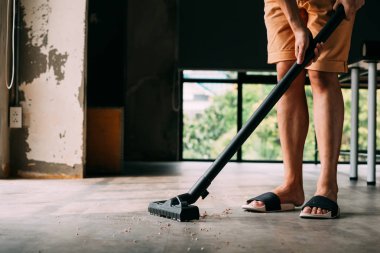 Evin içinde elektrikli süpürge kullanarak sandalet giyen insan bacakları