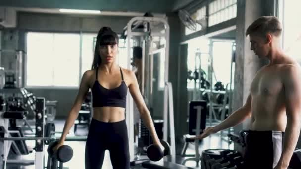Mulher magro dançando enquanto faz o lado lateral levantar exercício com seu personal trainer no ginásio — Vídeo de Stock