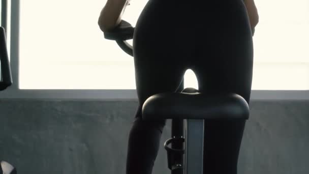 Вид сзади на спортивную женщину на стационарном велосипеде в тренажерном зале — стоковое видео