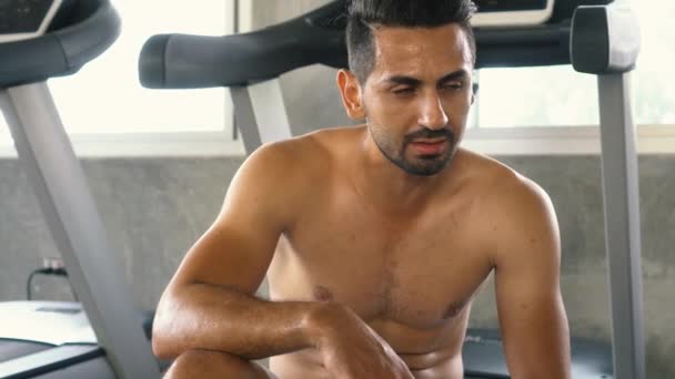 Tired man wiping sweat while relaxing after exercising at the gym — Stock Video