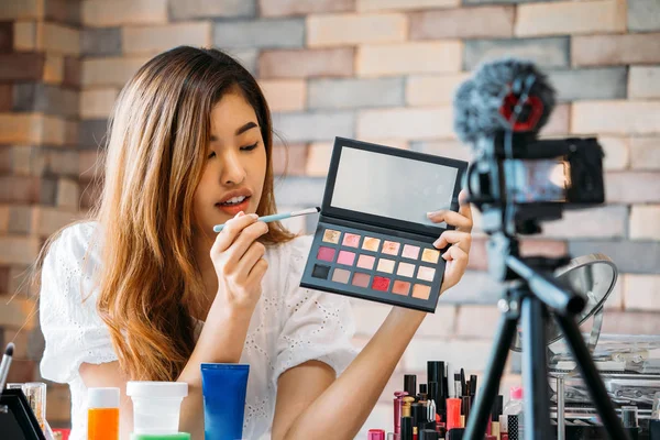 Mujer bastante asiática grabando vídeo tutorial de maquillaje sobre cosméticos con teléfono móvil en trípode — Foto de Stock