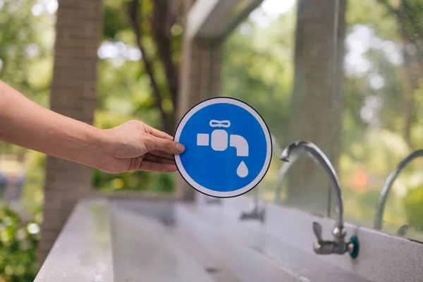 Αρσενικά χέρια που κρατούν μια μπλε πινακίδα βρύσης με τη βρύση του νερού βρύσης στο πάρκο — Φωτογραφία Αρχείου