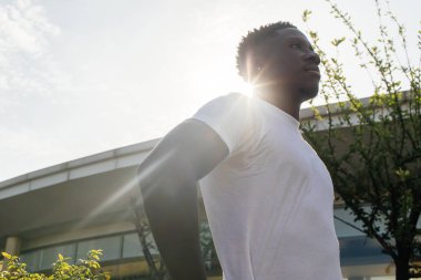 Kalçalarında elleri olan Afro-Amerikan adam evde gökyüzüne bakarak poz