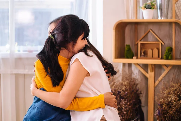 Улыбающаяся азиатская дочь обнимает свою мать в гостиной дома — стоковое фото