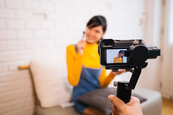 Joven mujer asiática sosteniendo cepillo de cosméticos mientras graba un video con cámara profesional —  Fotos de Stock