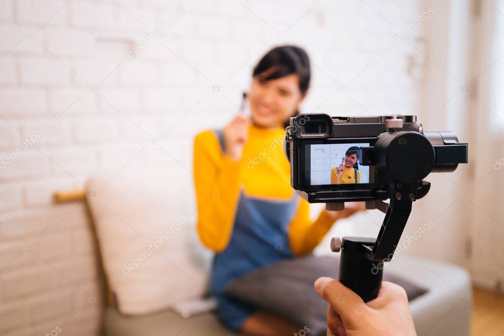 Young Asian woman holding cosmetics brush while recording a video with professional camera