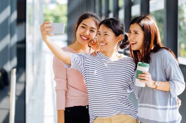 Genç Asyalılar cam binanın içinde birlikte selfie fotoğrafları çekiyor
