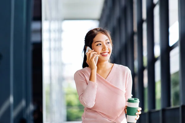 Joven mujer asiática hablando en el teléfono móvil en la oficina fondo exterior — Foto de Stock