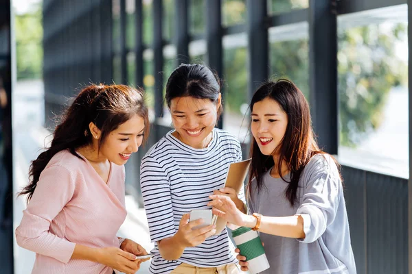 Молодые азиатские деловые женщины разговаривают и показывают экран телефона в офисном здании в повседневной одежде — стоковое фото
