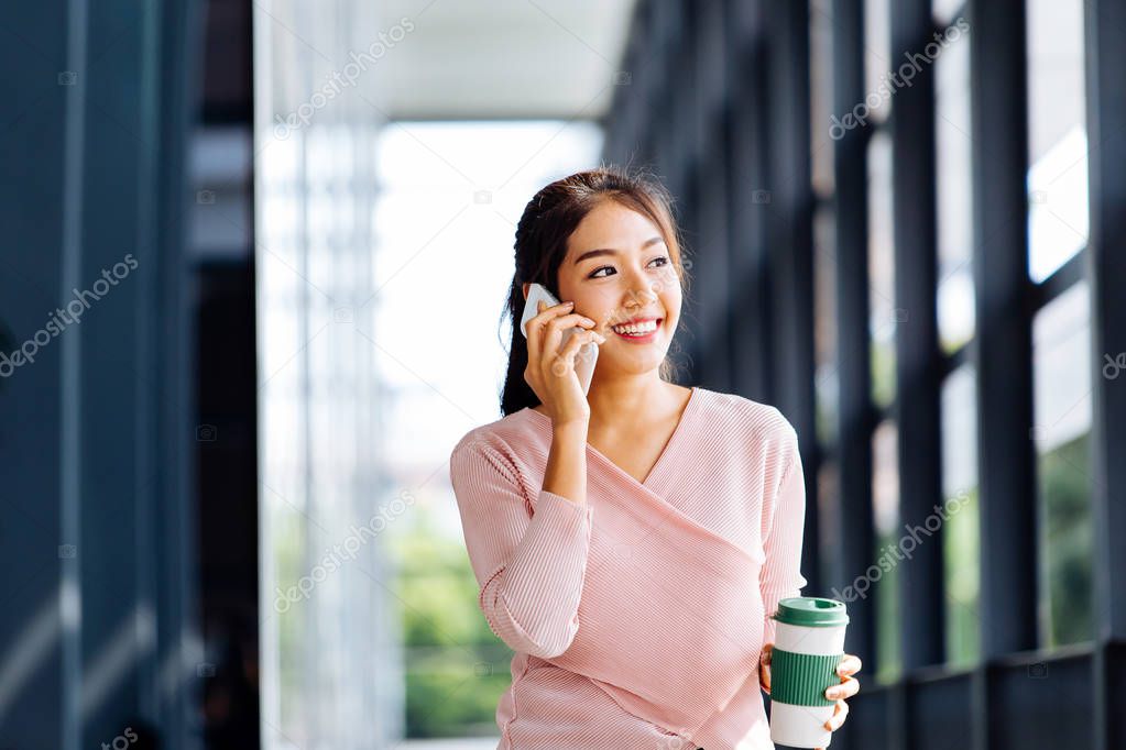 Young Asian woman talking on mobile phone at office exterior background