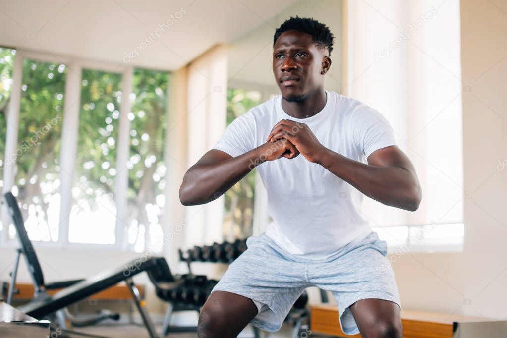 African American sportsman squatting in gym