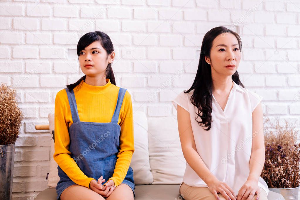 Displeased Asian females sitting on sofa