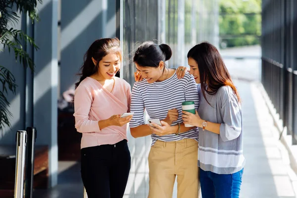 Jóvenes mujeres de negocios asiáticas hablando y mostrando la pantalla del teléfono en el edificio de oficinas en ropa casual — Foto de Stock