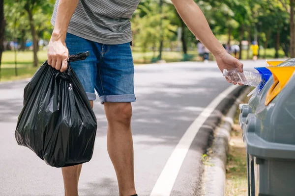 Feche a mão do homem jogando uma garrafa de plástico na lixeira. Classificação de lixo antes de colocar na lixeira — Fotografia de Stock