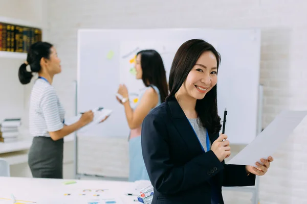 Asiatische Geschäftsfrau hält Stift und Papier in die Kamera während eines Meetings — Stockfoto