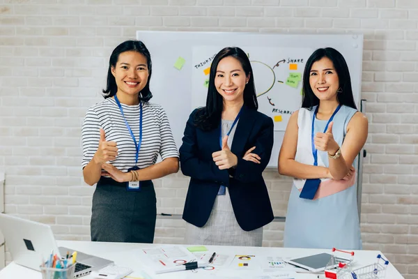 Sorridente asiatica giovani donne d'affari in abbigliamento casual in piedi in linea con i pollici in alto gesto in sala riunioni — Foto Stock