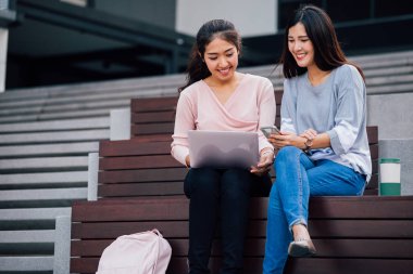 Asyalı öğrenciler dizüstü bilgisayar ve akıllı telefon ile oturan ve gülümseyerek