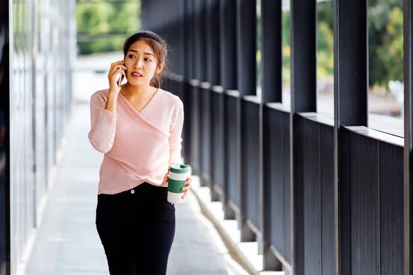 Mujer asiática con smartphone hablando y mirando junto con el café en la mano — Foto de Stock