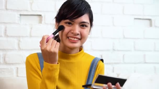 Adolescente asiática chica aplicando maquillaje mientras está sentado en el sofá — Vídeo de stock