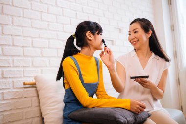 Kanepede otururken kızı makyaj yapan Pozitif Asyalı anne