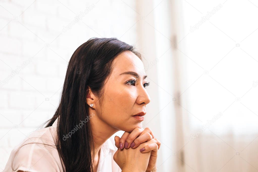 Mature Asian woman putting two hands together and praying at home
