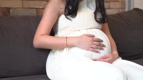 Беременная женщина трогает ребенка внутри живота на диване — стоковое видео