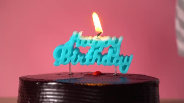 Joven soplando las velas azules en forma de Feliz Cumpleaños sobre fondo rosa — Vídeos de Stock