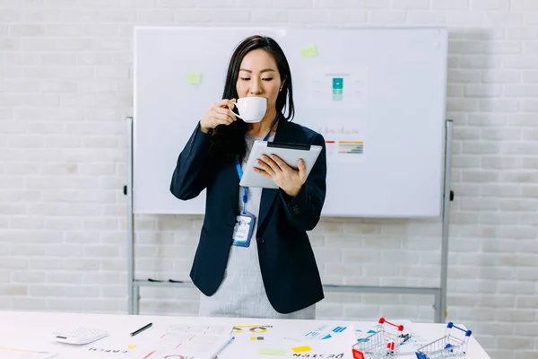 Atenta mujer de negocios asiática usando tableta mientras bebe café en la oficina — Foto de Stock