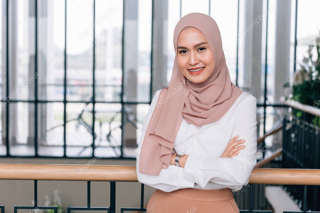 Young happy and successful South East Asian Islamic business woman with arms crossed in building