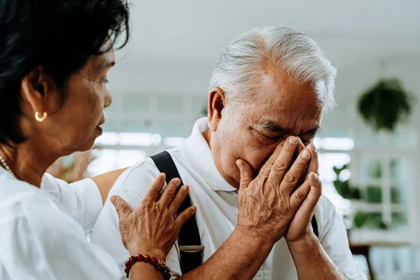 Mutsuz emekli Asyalı yaşlı çift koltukta otururken yaşlı kadın üzgün kocasını evinde teselli ediyor..
