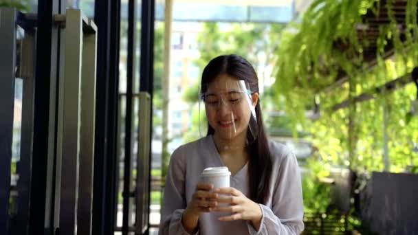 Young 20s Asian beautiful girl wearing a protective face shield and mask. Professional business woman holding a cup of coffee - Corona Virus prevention concept — Stock Video