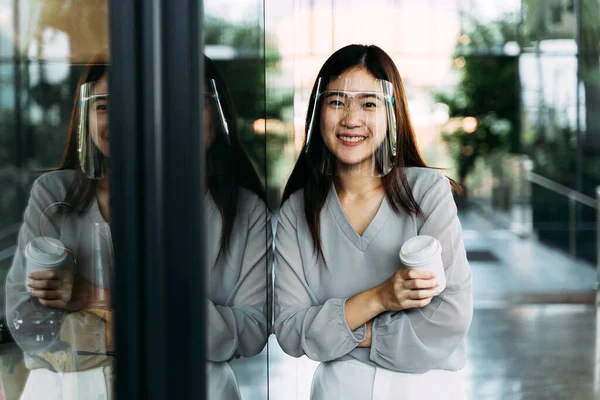 Young 20s Asian beautiful girl wearing a protective face shield and mask. Professional business woman holding a cup of coffee - Corona Virus prevention concept — Stock Photo, Image