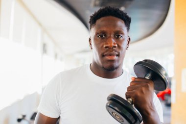 Genç Afrikalı Amerikalı adam spor salonundaki halterleri kaldırıyor ve ayakta duruyor.