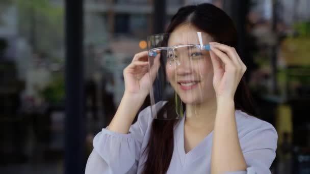 Jonge Aziatische vrouw opstijgen en tonen een gezicht schild bij coffeeshop — Stockvideo