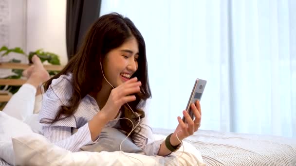 幸せな20代のアジアの女性がカジュアルな服装で自宅でスマートフォンでFacetimeのビデオ通話を作るの肖像画。会議オンラインアプリを使用して、,社会的距離,家庭の概念から仕事 — ストック動画