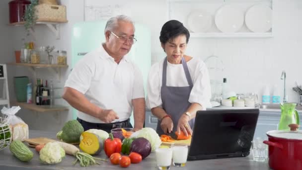 Старшая азиатская пара использует ноутбук во время приготовления пищи на кухне дома. 70-е годы Пожилые мужчина и женщина в отношениях пенсионного образа жизни концепции. — стоковое видео