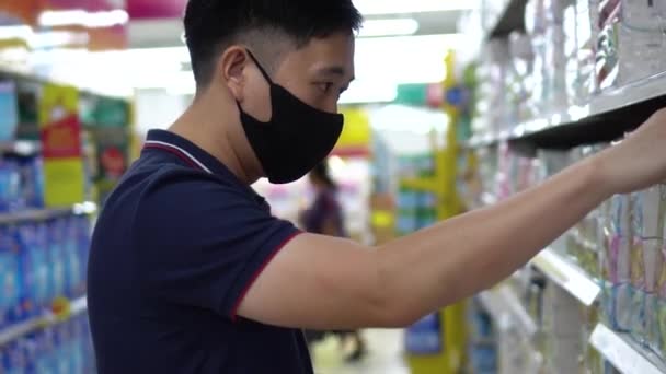 Pemuda Asia yang mengenakan masker wajah saat berbelanja dengan troli gerobak di supermarket — Stok Video