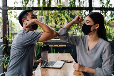 Asian woman and man friends wearing face mask outdoors. Friends greeting and shaking with elbows as new normal. Corona Virus - Covid 19 elbow bumps greeting style to prevent contact and virus spread clipart