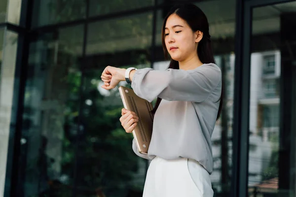 Азиатская деловая женщина проверяет часы возле офисного здания — стоковое фото