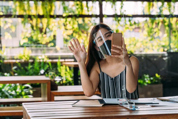 얼굴 가리개를 착용하고 테라스에서 휴대폰을 들고 미소짓는 행복 한 아시아 여성. Covid-19 기간의 비디오 통화 기술 - 코로나 바이러스 — 스톡 사진