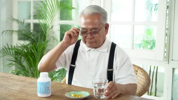 Homme asiatique âgé prenant la pilule avec une tasse d'eau à la maison — Video