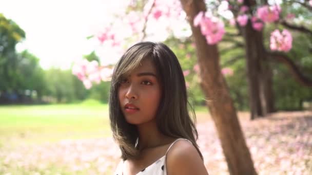 Mujer hermosa joven pensando y mirando hacia otro lado en el parque. Linda chica ausente de la mente de pie en el jardín de flores . — Vídeos de Stock