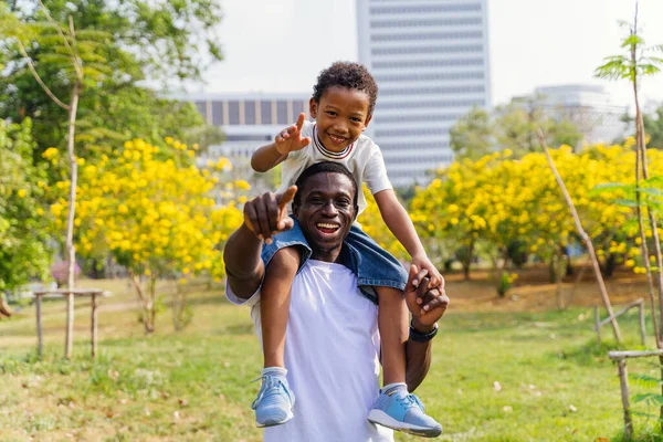 Afrikalı Amerikalı baba ve oğul parkta sırtına binmiş. Babalık ve mutlu aile hayatı kavramı — Stok fotoğraf