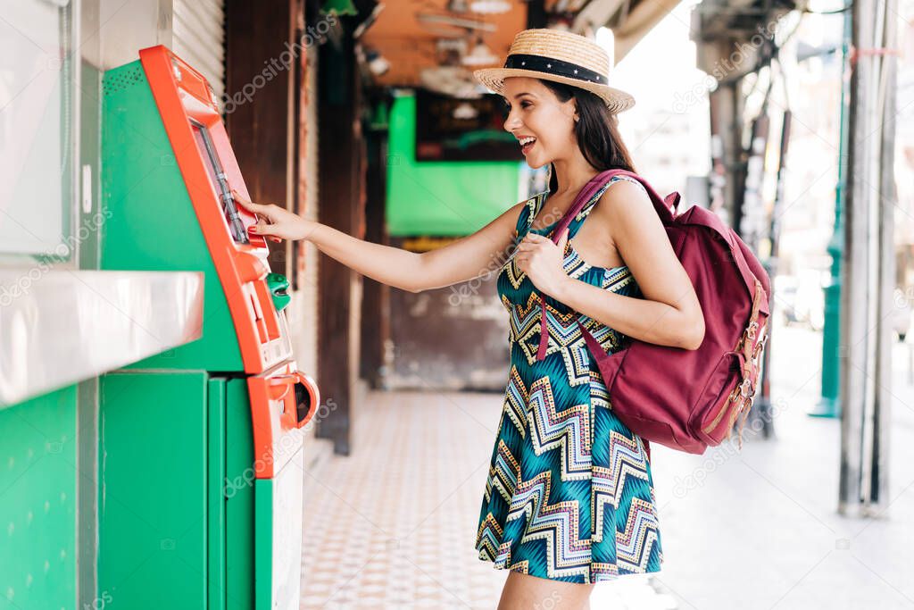 Young brunette girl traveler withdrawing money from ATM in Thailand, Asia.