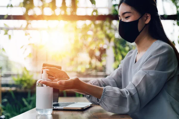 Jovem de 20 anos mulher bonita asiática com sorriso atraente usando gel higienizador de mão para lavar as mãos. Ao usar laptop de computador e telefone celular fora na cena do café. - Conceito de prevenção de vírus Corona — Fotografia de Stock